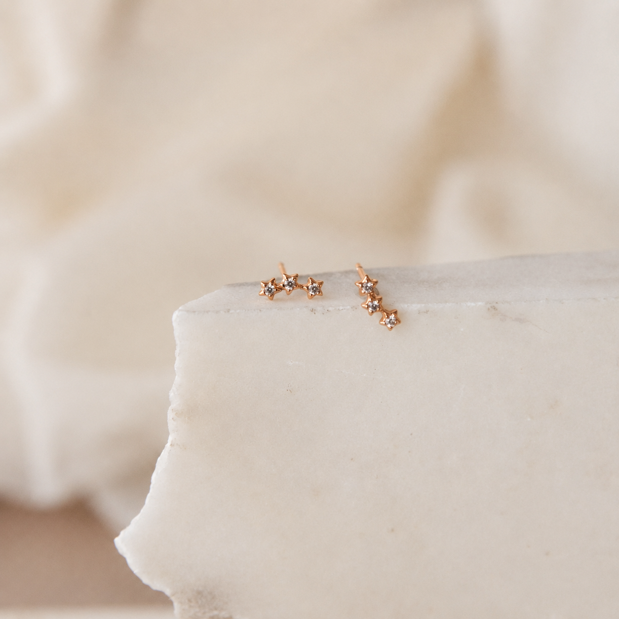 Rose gold star-shaped earrings on a white cushion with a soft beige background